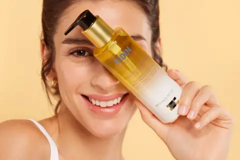 Mujer sonriente sostiene una botella de aceite de ducha ISDIN.