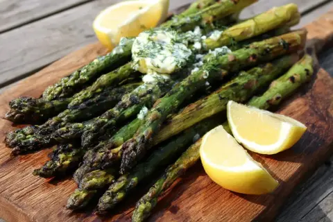 Grilla sparris med smör och dill, serverad med citronklyftor på en träskärbräda. Perfekt sommarbuffé!
