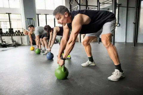 Gruppe trainiert Griffkraft mit Kettlebells. Sie heben die Gewichte vom Boden, um ihre Hände zu stärken.