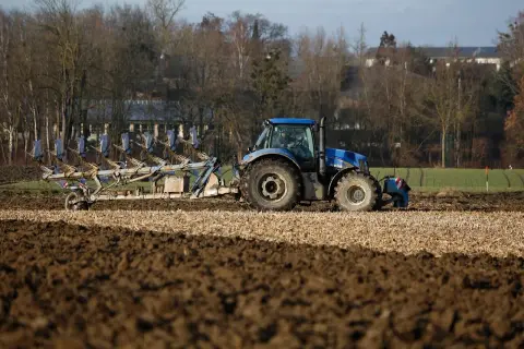 Niebieski traktor z pługiem orze pole. Rolnik przygotowuje ziemię, zastanawiając się, do kiedy można orać pole arimr.