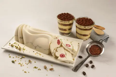 Delikatny krem do tortu z mascarpone, udekorowany malinami i pistacjami, obok deserów tiramisu.