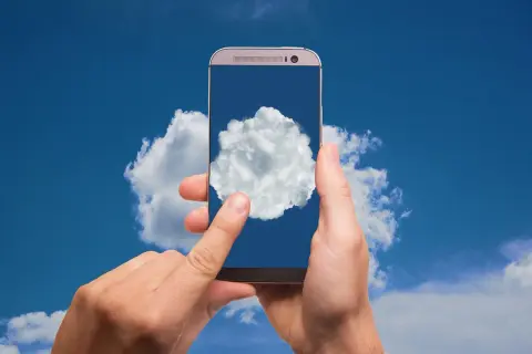 Dłonie trzymają smartfon, na którego ekranie wyświetla się chmura. To symbol nowoczesnej usługi chmura, dostępnej zawsze pod ręką.