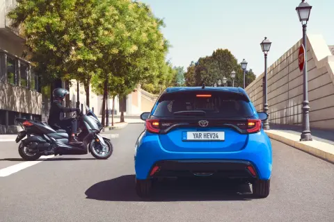 Niebieski Toyota Yaris HEV. Kierowca na skuterze obok. Szukasz "toyota yaris instrukcja obsługi po polsku"?