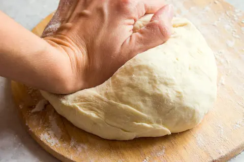 Main d'une personne pétrissant une pâte à pain sur une planche en bois. Une question se pose : pourquoi ma pâte ne lève pas ?