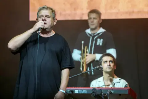 Kultowi artyści na scenie. Wokalista z mikrofonem, w tle trębacz i klawiszowiec. Ich kultowe utwory poruszają serca.