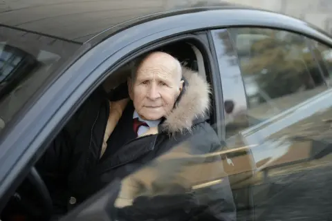 Un homme âgé, au regard vif, est assis au volant de sa voiture, prêt à prendre la route. Son permis de conduire senior lui permet de garder son indépendance.