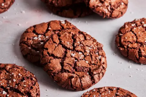 Knusprige brownie cookies mit Meersalzflocken, die auf einer hellen Oberfläche liegen.