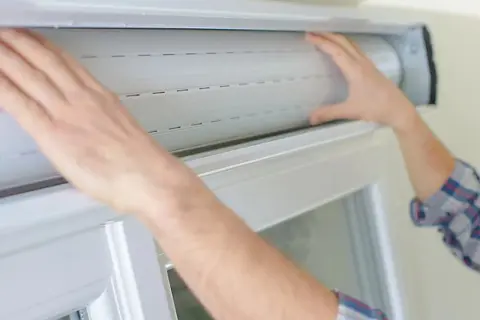Mains manipulant un volet roulant blanc, étape clé pour savoir comment réparer un volet roulant.
