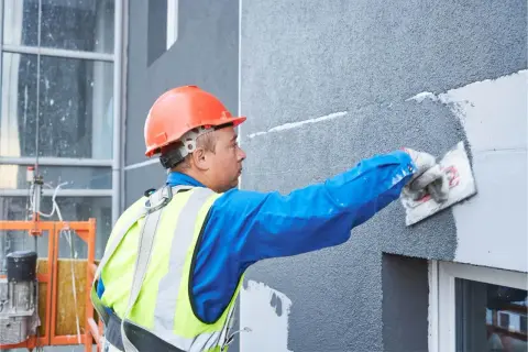 Obrero con casco naranja aplica mortero para como aislar una fachada exterior.
