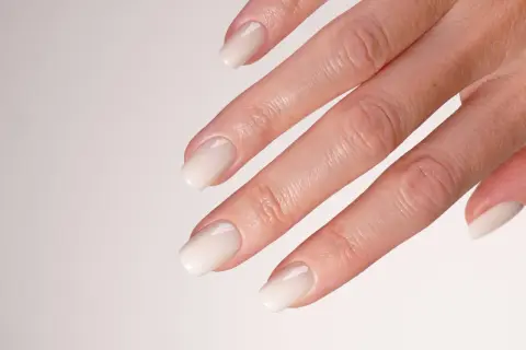 Mano con unghie sposa eleganti, laccate di un bianco perla, perfette per il giorno più bello.