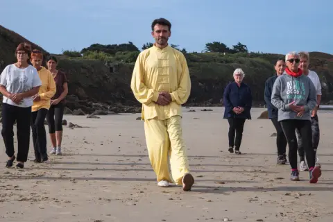 Un groupe suit un homme en tenue jaune lors d'une marche afghane sur une plage.