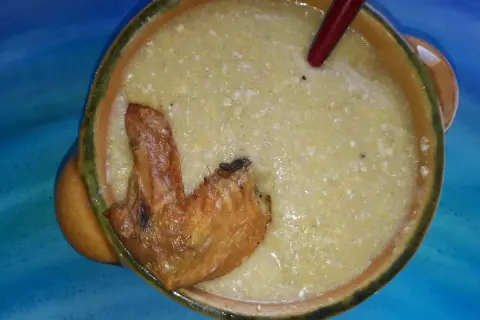 Herzhafte polenta taragna mit einem knusprigen Hähnchenflügel in einer rustikalen Schüssel.