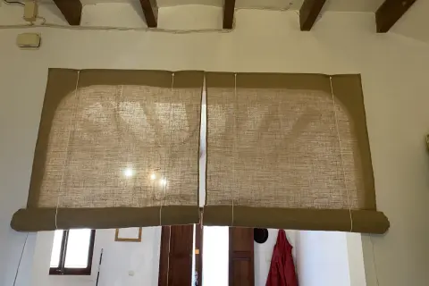 Dos estores enrollables caseros de tela de yute cubren una ventana. La luz del sol se filtra a través de ellos.