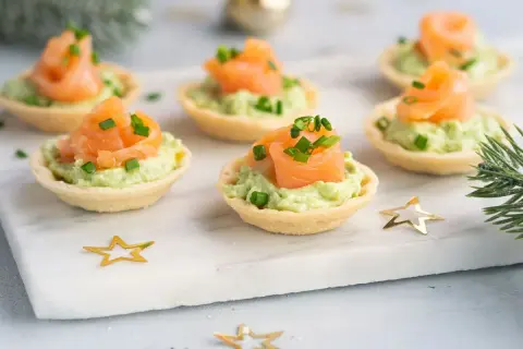 Aperitivos baratos para mucha gente: canapés de salmón y aguacate, decorados con cebollino y estrellas doradas.