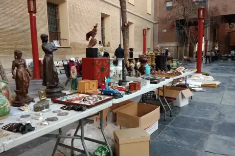 Mercado de antigüedades en Zaragoza con estatuas, jarrones y objetos curiosos en mesas al aire libre.
