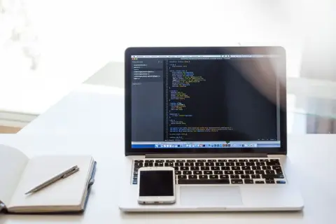Laptop z kodem, telefonem i notatnikiem. Dobry laptop powinien mieć odpowiednie parametry do pracy.
