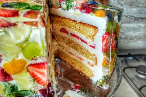 Kolorowy tort z galaretką i owocami, przekrojony, ukazujący warstwy biszkoptu i kremu.