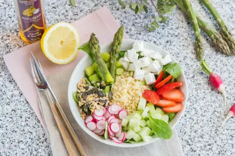 Un plat végétarien coloré avec du quinoa, des asperges, des fraises, du concombre, des radis, des graines et du fromage feta.
