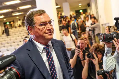 Mężczyzna w garniturze, jak kapitan reprezentacji Polski, otoczony przez fotoreporterów z aparatami.
