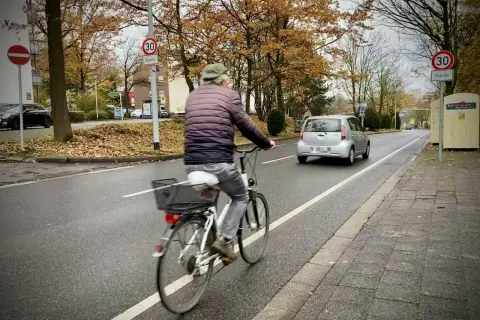 Mann fährt Rad auf einem geschützten Radweg. Ein Auto fährt auf der Straße.