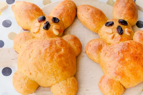 Zwei goldbraune Osterhasen aus Hefeteig, dekoriert mit Rosinen und Mandeln. Perfekt zum Osterbacken mit Kindern.
