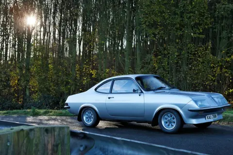 Silver Vauxhall Firenza på en väg kantad av träd. Solen skiner genom grenarna.