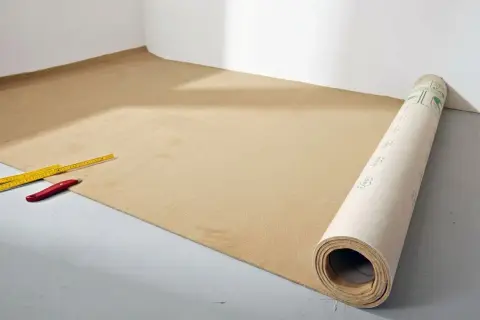 Werkzeug liegt bereit für das Teppich verlegen. Ein Teppichboden wird ausgerollt, daneben ein Zollstock und ein Cuttermesser.