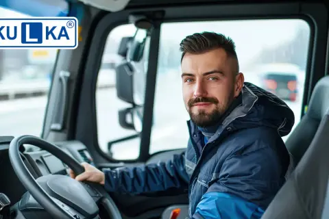 Uśmiechnięty kierowca ciężarówki, świadomy ważności prawa jazdy, siedzi za kierownicą. Na szybie widoczny znak "KULKA".