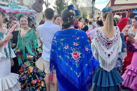 Mujeres con trajes de flamenca y mantones bordados, uno azul con flores rojas y otro blanco con detalles coloridos.