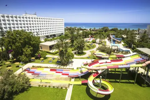 Kolorowy aquapark na plaży w Saharze, z hotelowcem w tle i błękitnym morzem.