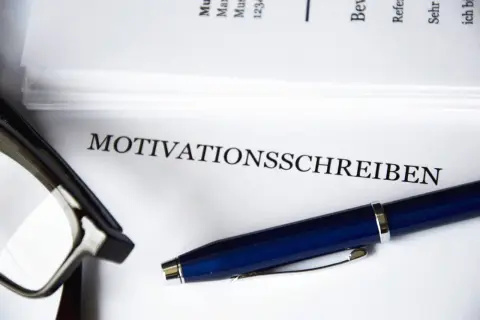 Okulary i długopis leżą obok dokumentu z napisem "MOTIVATIONSSCHREIBEN".