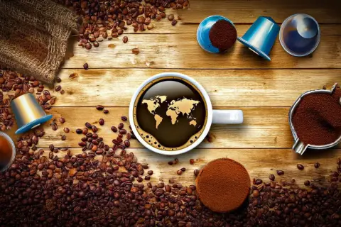 Tipi di cialde caffè e chicchi sparsi su un tavolo di legno. Una tazza di caffè con la mappa del mondo riflette il tema globale.