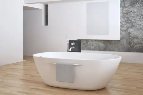 Eine freistehende **Badewanne mitten im Raum** auf hellem Holzboden, daneben ein moderner Wasserhahn und eine graue Handtuchhalterung.