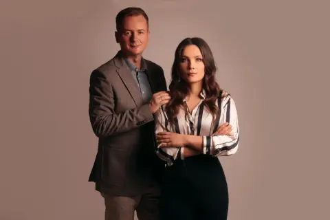 Mężczyzna w garniturze i kobieta w bluzce w paski stoją obok siebie.
