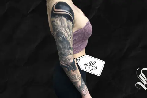 Ein beeindruckendes, all black tattoo ziert den Arm einer Frau. Ein Löwe blickt majestätisch, umgeben von Rosen und abstrakten Formen.