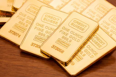 Sztabki złota Credit Suisse, każda o wadze jednej uncja trojańska, błyszczą na drewnianym tle.