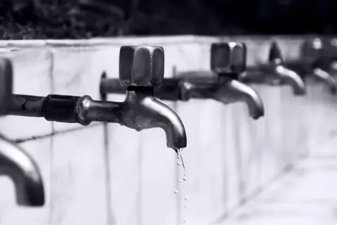 Reihe von Wasserhähnen, aus denen Tropfen fallen.