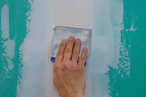 Main d'un artisan ponçant un mur à la main avec une spatule pour lisser le plâtre.