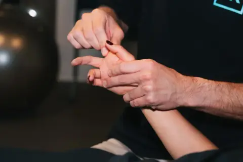 Un thérapeute manipule délicatement un doigt, peut-être pour traiter une luxation.
