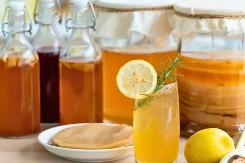 Verre de kombucha rafraîchissant, entouré de bouteilles et de bocaux, rappelant l'origine pays de cette boisson fermentée.