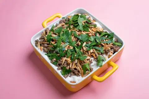 Un plat de fatteh aubergine garni de viande hachée, d'amandes effilées et de persil frais, dans un plat jaune à pois blancs.