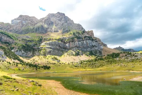 El ibón Piedrafita, un espejo de agua sereno, refleja la majestuosidad de las montañas rocosas y verdes.