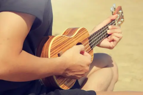 Person spielt auf einer Ukulele, die Hände formen den D-Dur-Akkord. Die Holzmuster der Ukulele sind gut sichtbar.