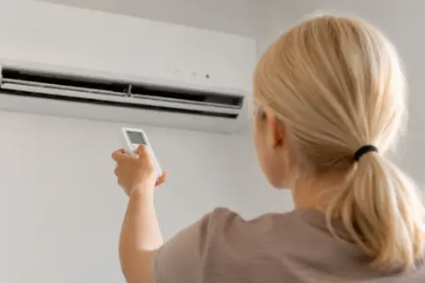 Donna bionda con telecomando davanti a un condizionatore. Guida su come scegliere condizionatore.