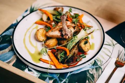 Pyszne danie z kurczaka z ziemniaczkami i marchewką, ozdobione ziołami. Idealna pozycja z **Fischgarten menu**.