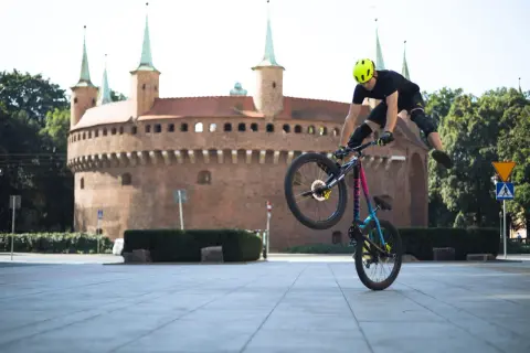 Kaskader na rowerze wykonuje trik przed Barbakanem w Krakowie. To niesamowity pokaz velo kraków!