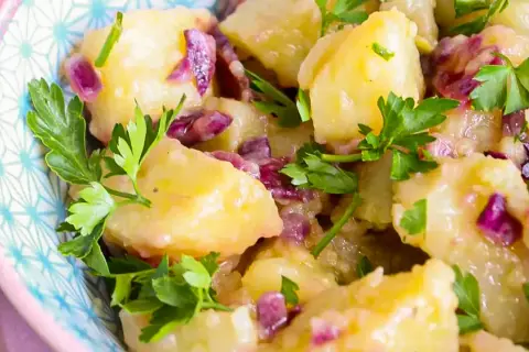 Salade de pommes de terre avec oignons rouges et persil frais dans un bol décoratif.