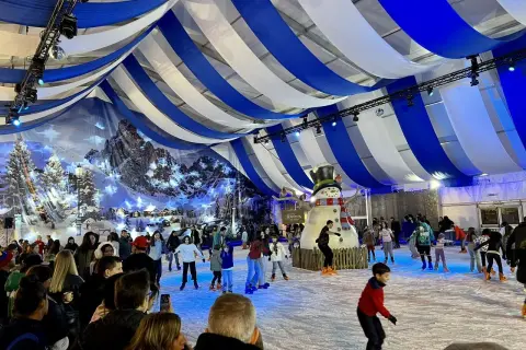 Pista de hielo en Zaragoza, Plaza del Pilar, con un gran muñeco de nieve y gente patinando bajo un techo de telas azules y blancas.