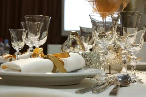 Service plat sur table avec des verres en cristal, des serviettes blanches nouées de ruban doré et des décorations scintillantes.