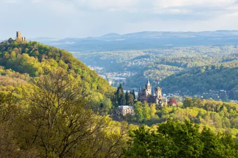 Majestätische Burg Drachenfels thront über einem grünen Tal mit einem Fluss und weiteren Burgen.